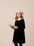 Menina com boina bege e vestido de veludo preto a segurar um livro