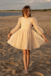Menina com vestido de cerimónia bege Holly a rodopiar na praia ao pôr do sol
