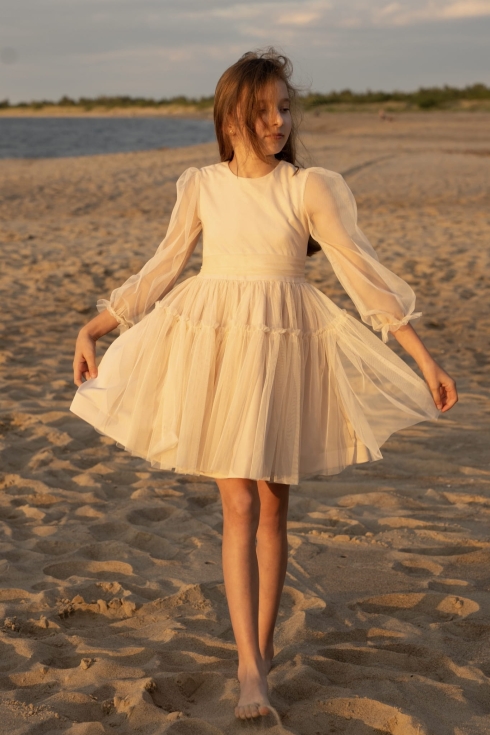 Menina com vestido de cerimónia bege Holly a rodopiar na praia ao pôr do sol