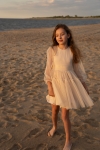 Menina com vestido elegante bege Holly a caminhar descalça na areia