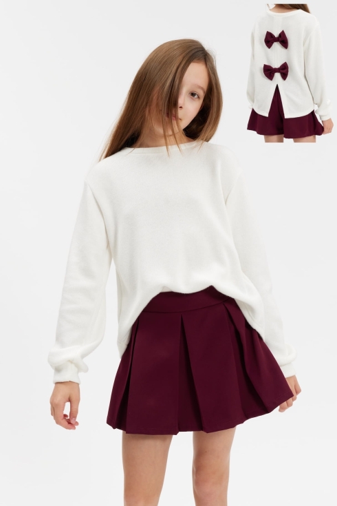 Menina de costas com conjunto Lia, camisola cru aberta atrás e dois laços bordô sobre saia-calção bordô