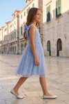 Vestido de cerimónia Rina azul-pervinca – menina numa rua da cidade antiga, silhueta completa de perfil