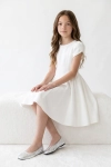 Vestido de cerimónia Rumi branco – menina sentada num banco branco, vista de frente
