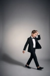 Fato de cerimónia Sam preto com laço – menino em movimento sobre fundo cinzento, blazer aberto, silhueta completa